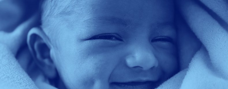 特写的婴儿婴儿裹着毯子和微笑,蓝色的过滤器。