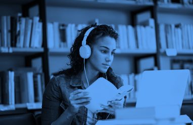 年轻女子戴着耳机手里拿着一本书学习,蓝色的过滤器。